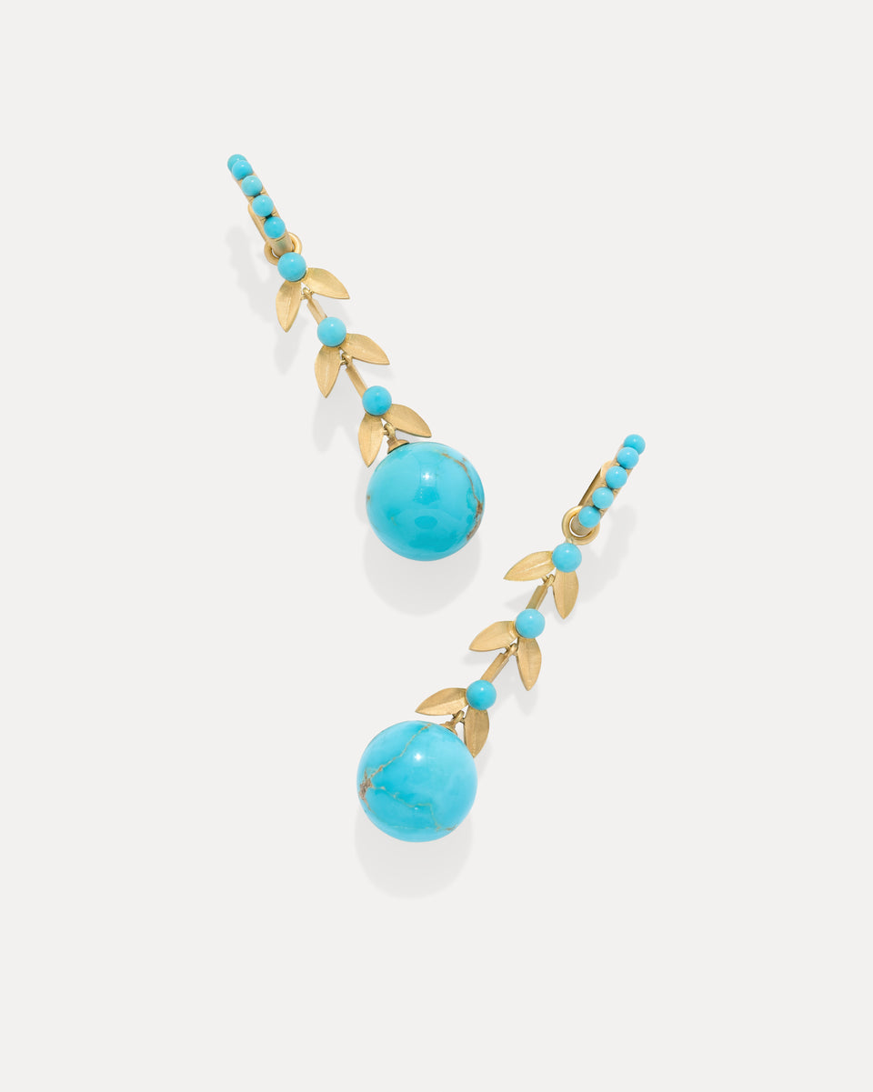A pair of gold drop earrings featuring large round turquoise blue beads, small turquoise beads, and gold leaf-shaped details, displayed on a light gray background.